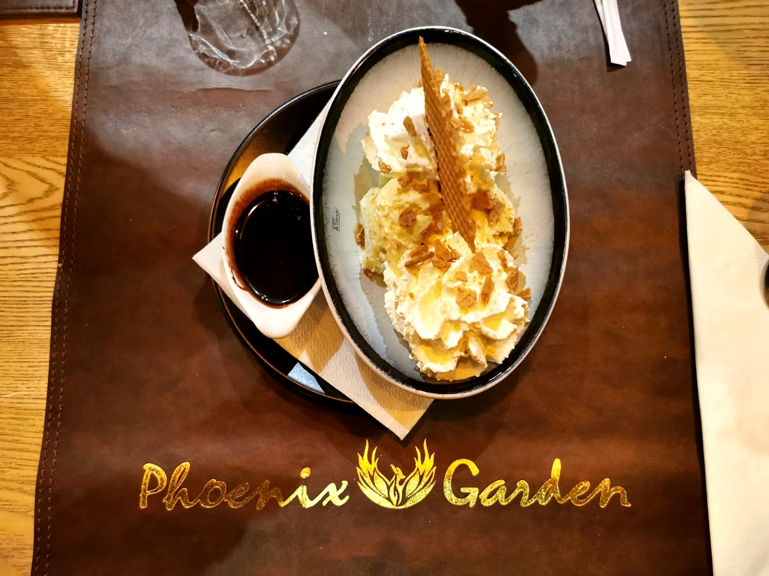 Dessert met room, ijs, chocolade en wafel boven het gouden Phoenix Garden-logo.