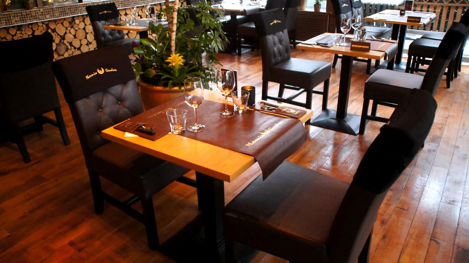 Gedekte tafel in de eetzaal van Phoenix Garden met leren stoelen, glaswerk, planten en houten vloer.